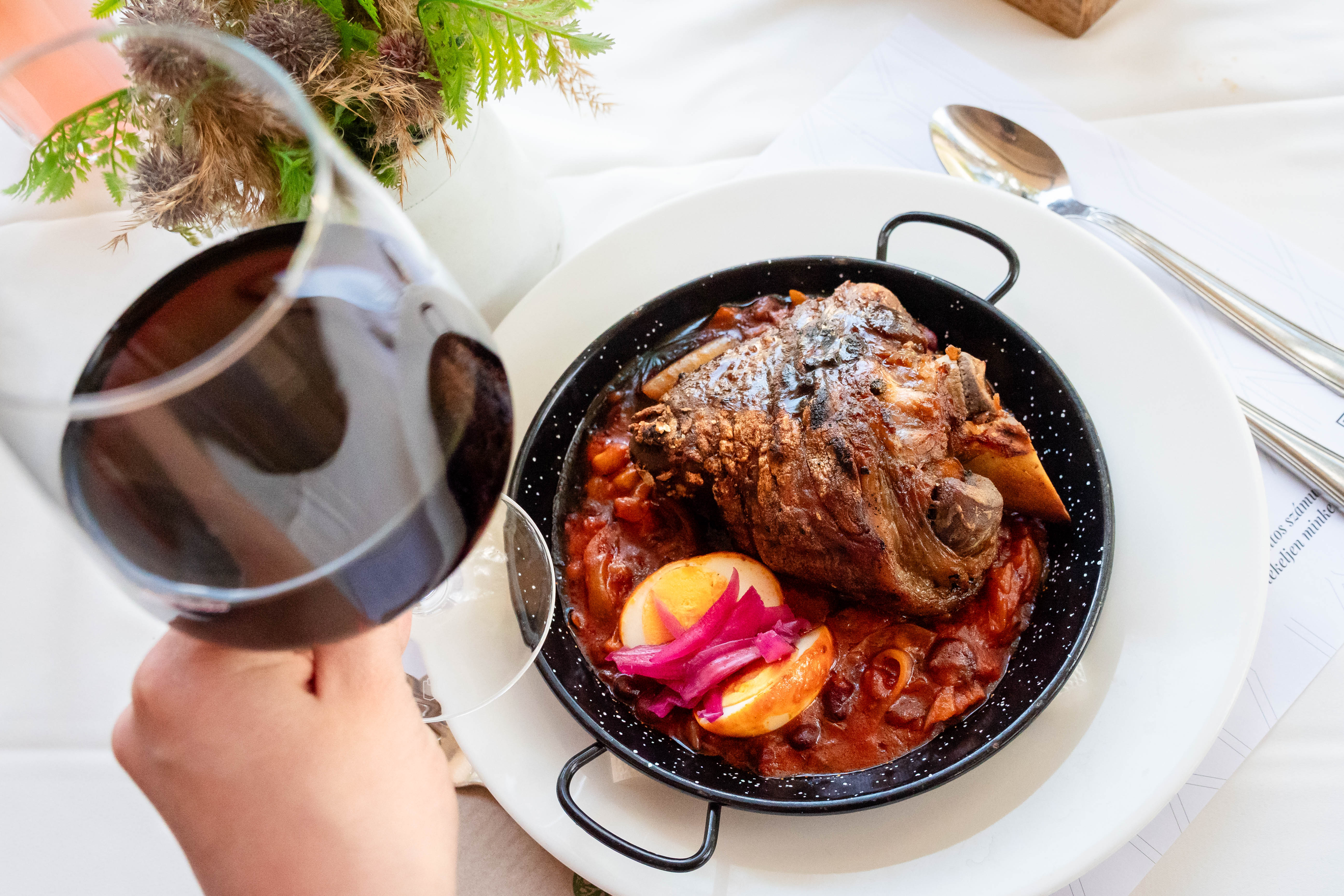Tálban tálalt babos csülök egy pohár vörösborral a Hotel Tókert asztalán, a Csülök Napok egyik ikonikus fogása.